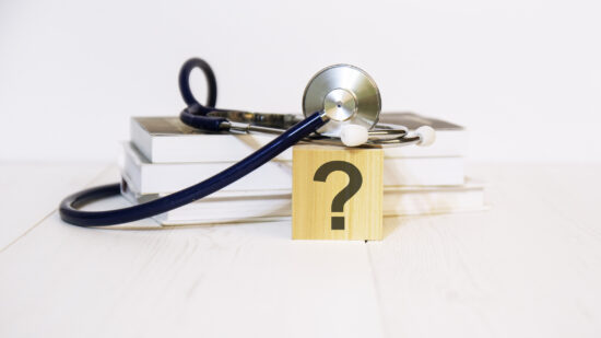 wooden block with question mark, stethoscope, book, notepad on white wooden table. medical and education concept