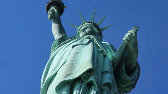 Low angle photo looking up at the Statue of Liberty against a clear blue sky. The photo emphasizes her tablet, crown, and torch.